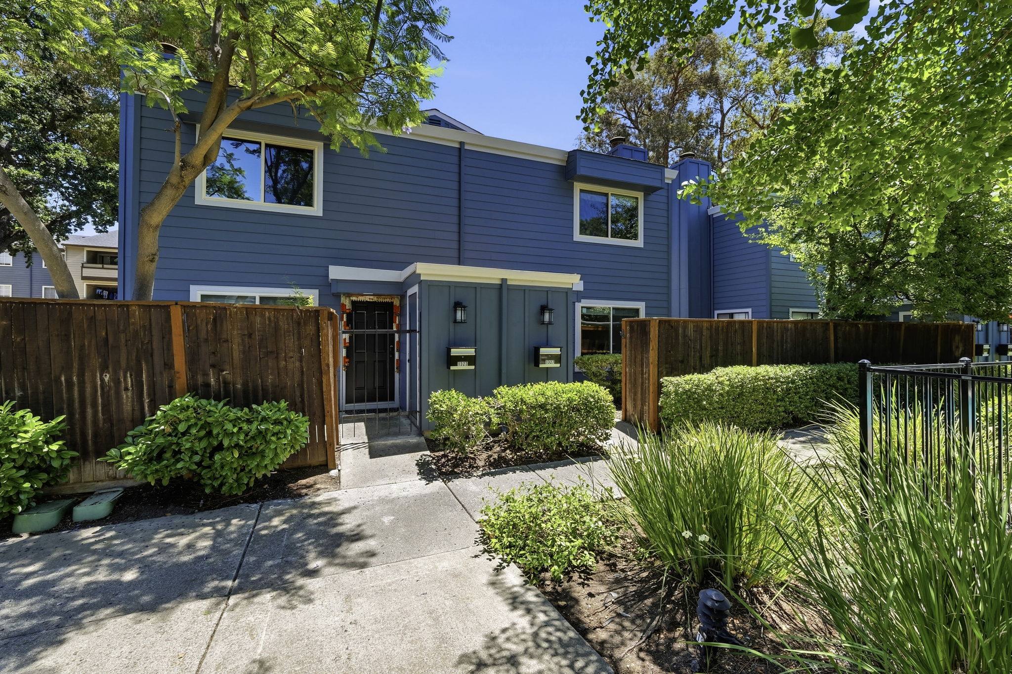 A blue Bay Vista–managed townhome framed by mature trees and trimmed hedges.